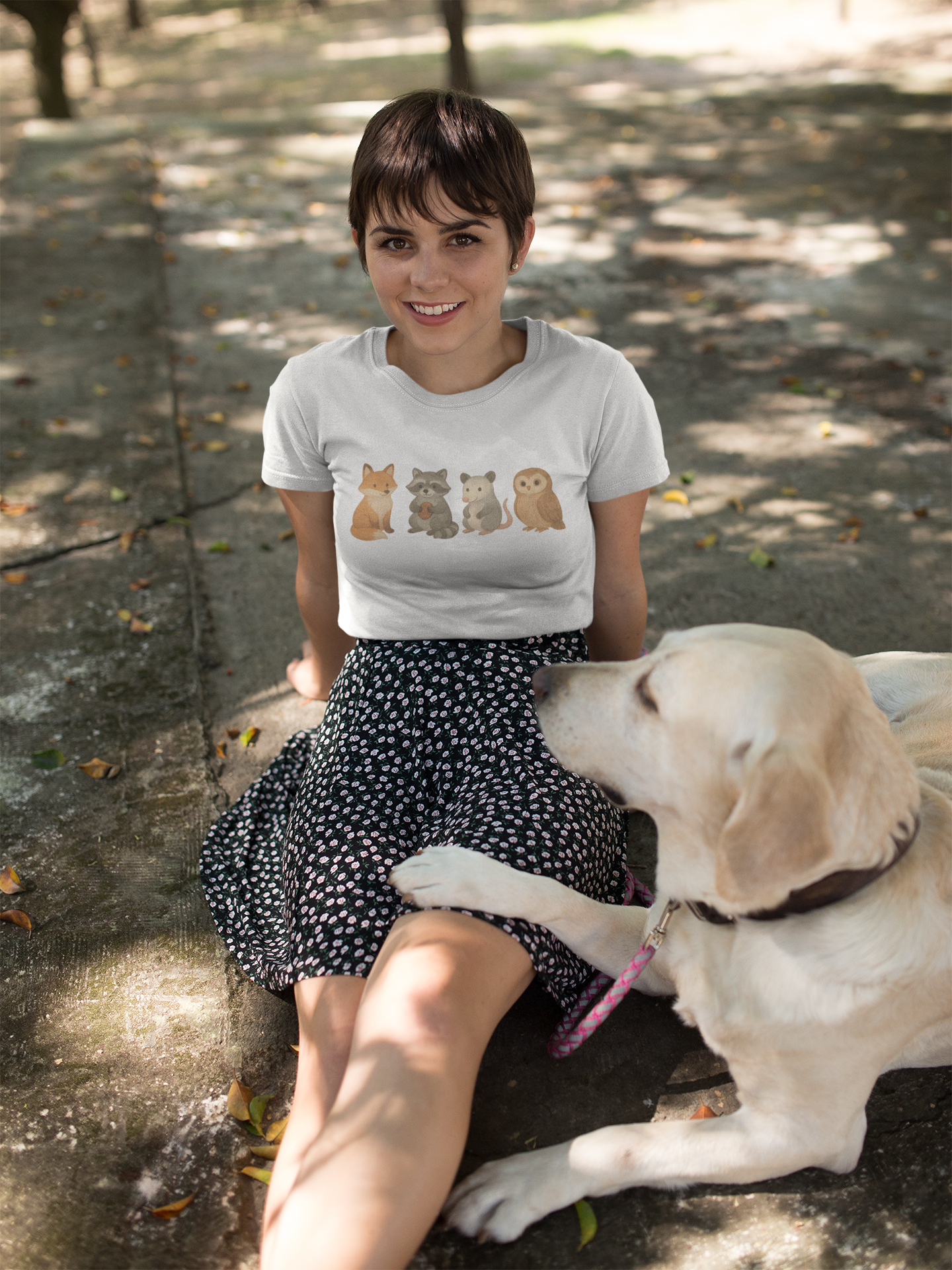 Woman sitting outdoors wearing an illustrated animal t-shirt with a labrador beside her – playful graphic tee for pet lovers